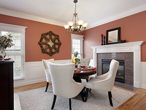 Orange feature room with bronze chandelier and fireplace with white chairs and dark wooden table